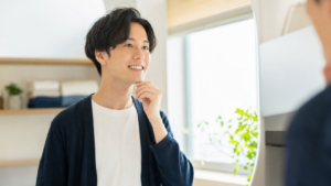 鏡の前で自然に笑う若い男性。歯列矯正で印象が変わるイメージ