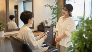 非リア充の人が美容室でスマホの髪型参考画像を見せながら相談している様子