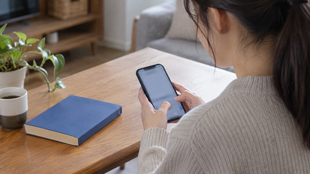 机の本を見ながらスマートフォンで連絡を準備する手元