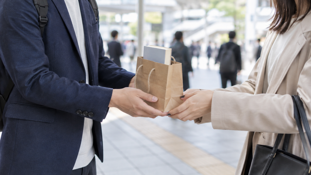 駅前で本の入った袋を短い受け渡しで受け取る二人
