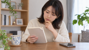 傷んだ借り物の本を前に連絡方法を考える女性