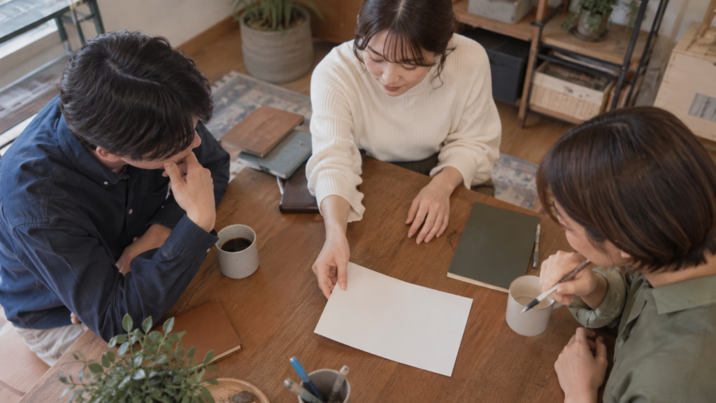 合同チームが資料を中央へ置き情報を共有する架空の説明イメージ