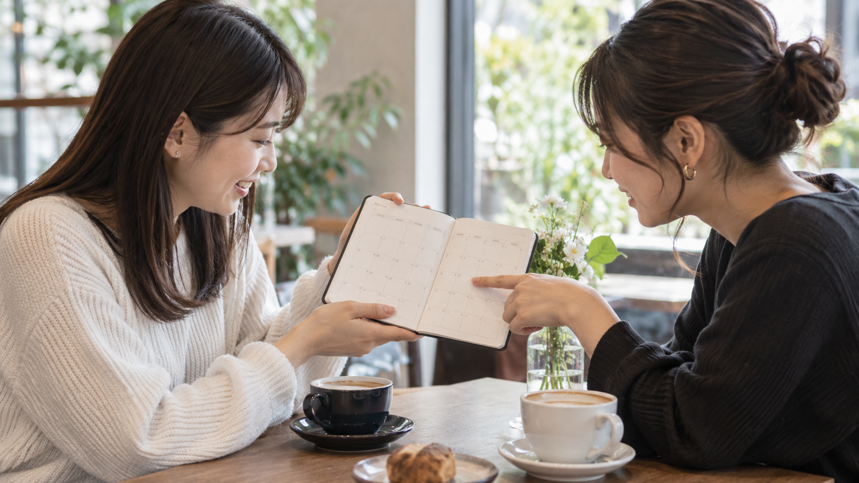 カフェで手帳を見ながら一緒に日程を相談する二人の友人