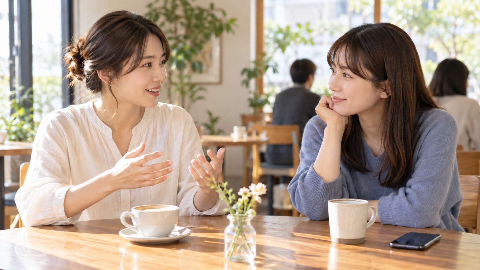 スマホを伏せてカフェで向かい合い会話する友人二人