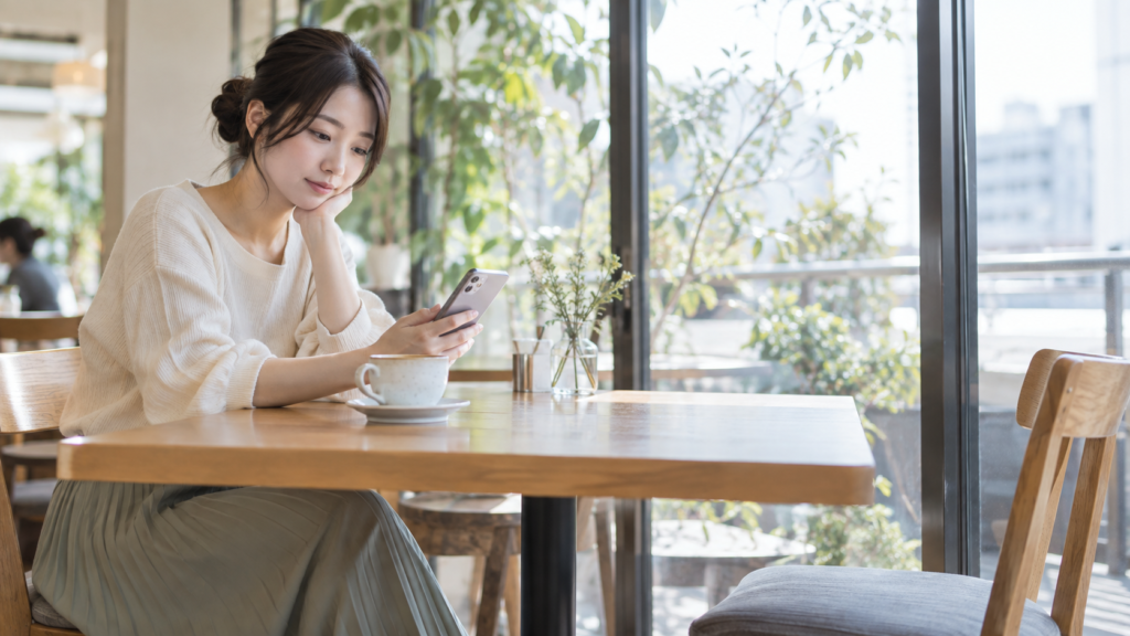 カフェの空いた向かい席を前にスマートフォンを確認する女性