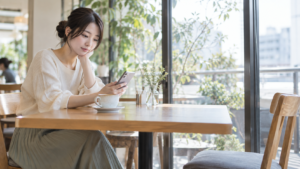 カフェの空いた向かい席を前にスマートフォンを確認する女性