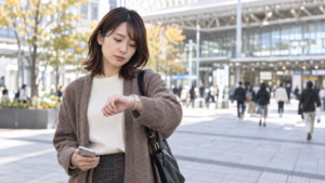 駅前で腕時計を見て友達の到着を待つ女性