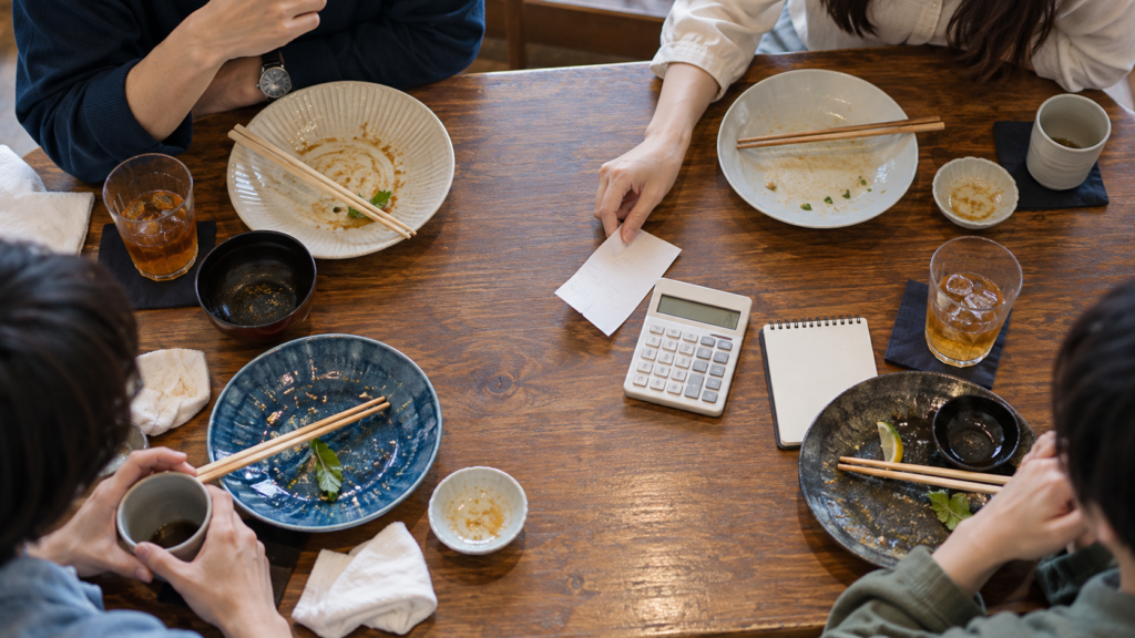 四人分の食事の後にレシートと電卓をそろえる様子