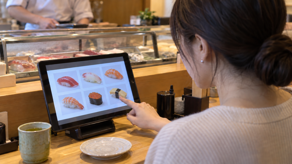 寿司店の注文端末を確かめる一人客のイメージ